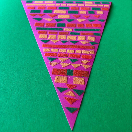 Colourful sand arranged in precise geometric patterns on a triangular green card