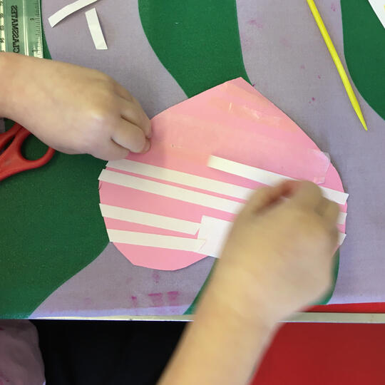 Hands peeling off double sided tape layer stuck onto pink heart laid on table with tablecloth