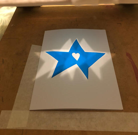 A5 card printed with blue star with white heart in the middle on wooden board shadows on the star