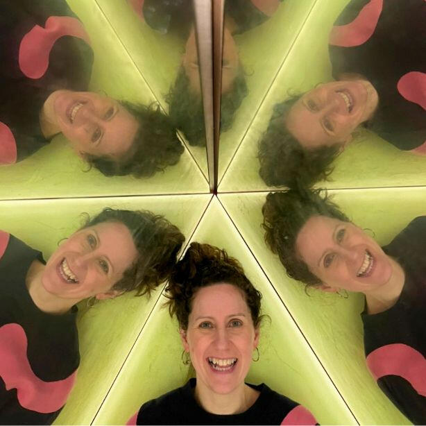 Lucie from Pattern & Print Club smiling in a hall or mirrors with the reflection in the mirrors