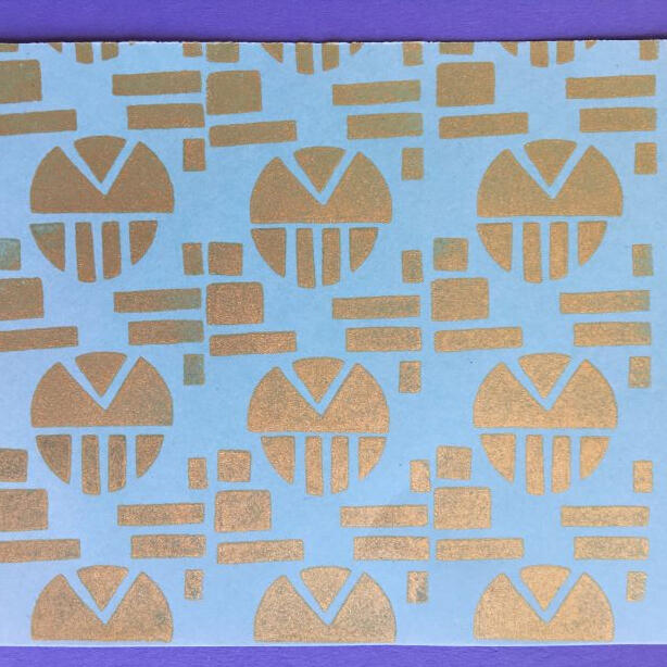 Gold printed stamp repeat pattern circle, rectangle and triangle designs on light blue paper.