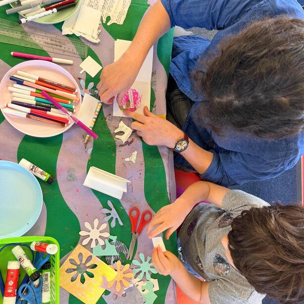 Adult and child together cutting, sticking and decorating with colourful paper, bright pens and craft supplies.